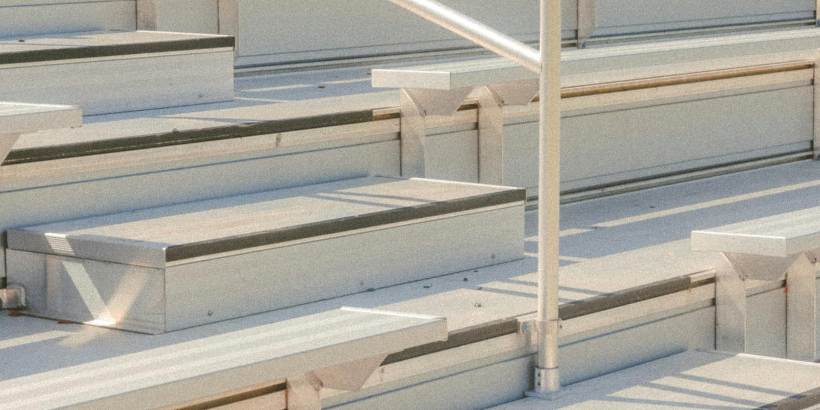 Empty aluminum bench bleachers in raking afternoon light.