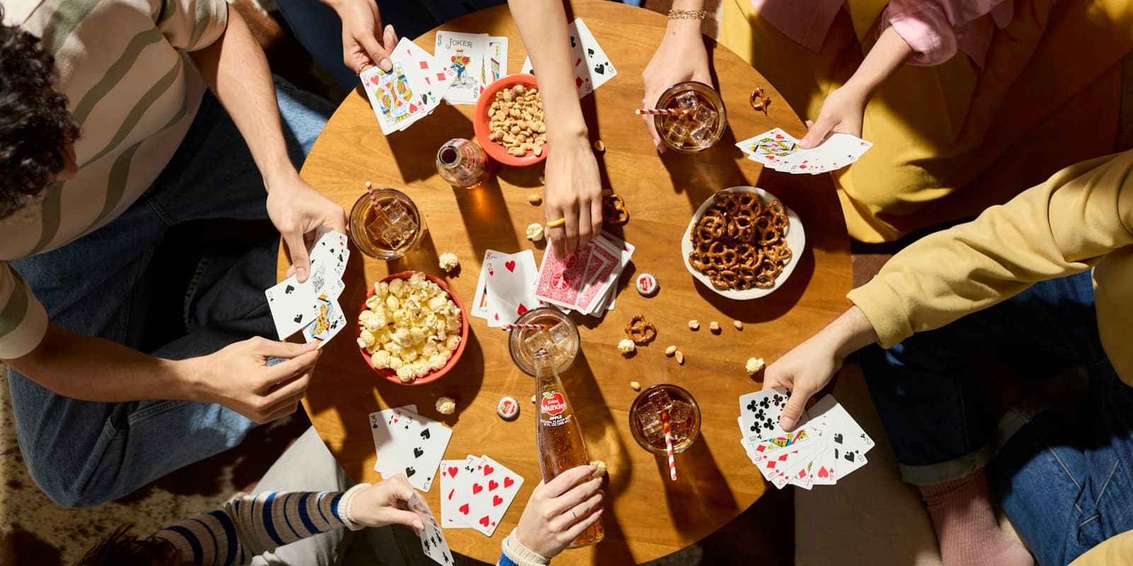 Overhead view of friends around a table mid-game, cards and snacks everywhere.